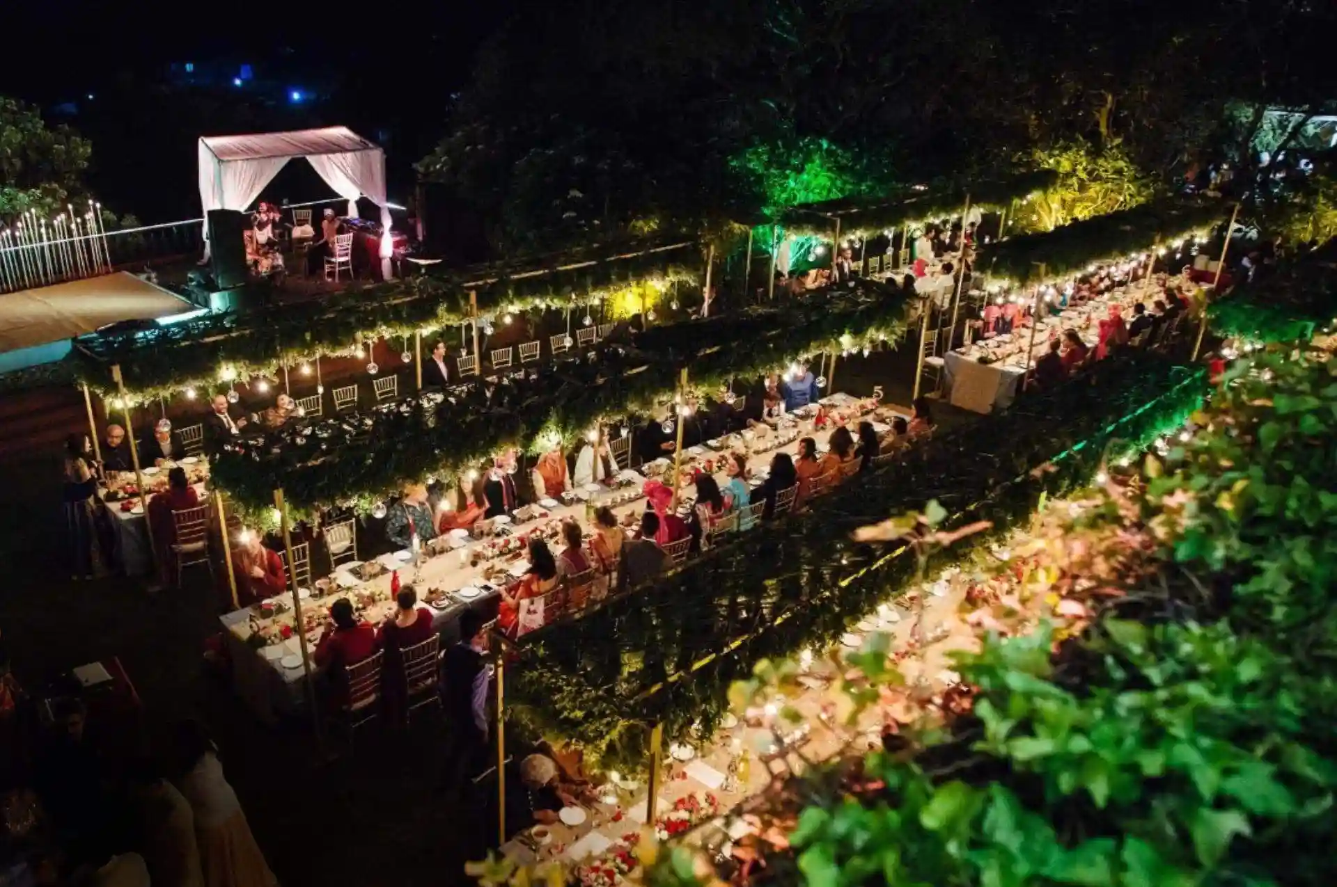 Ramsukh Resorts lawn with a long sit-down dinner arrangement lit with string lights for a night event.